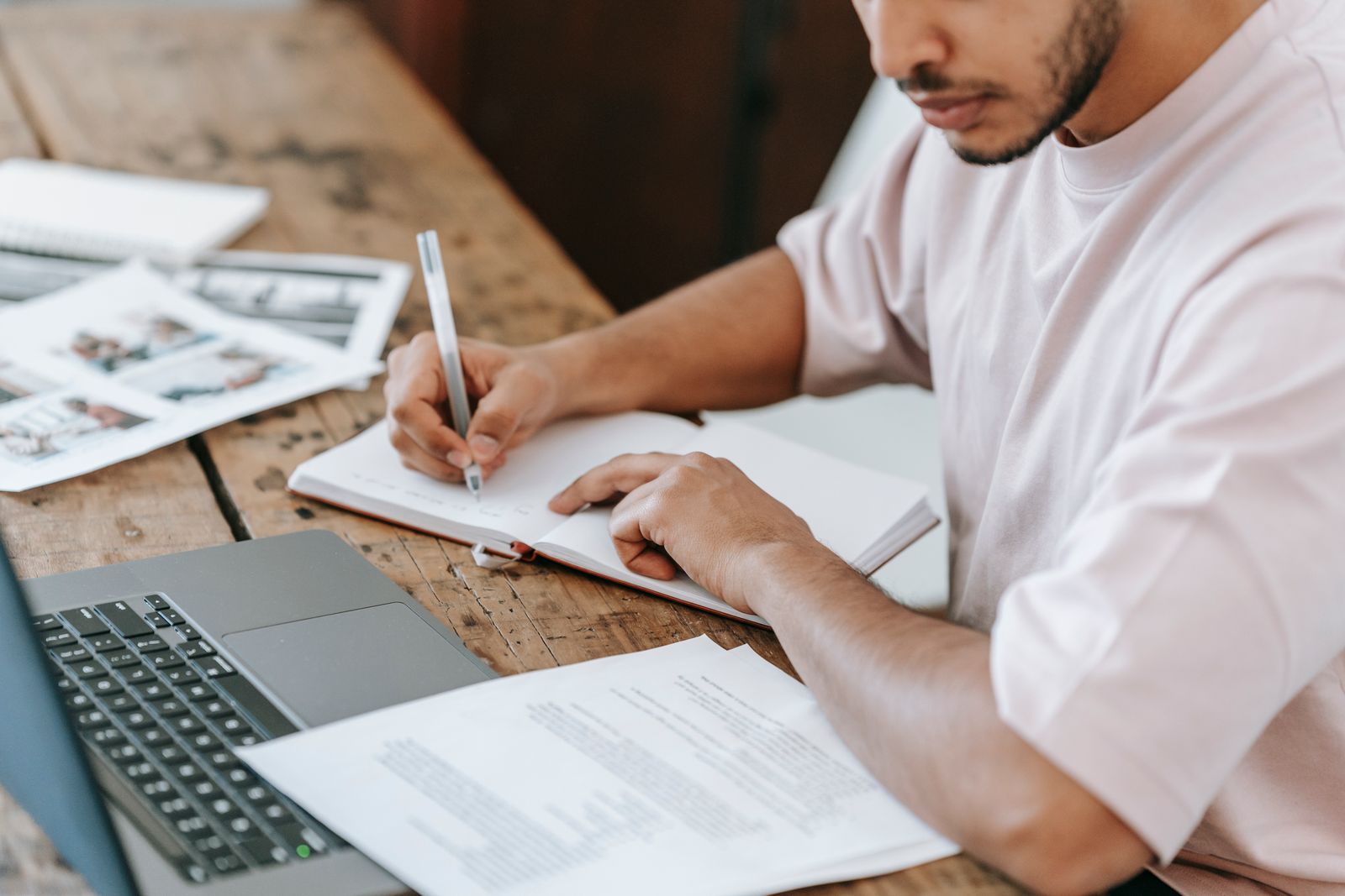 A student writing in an agenda at a desk with study papers and a laptop.